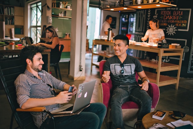 Two men talk as they work on a laptop computer.