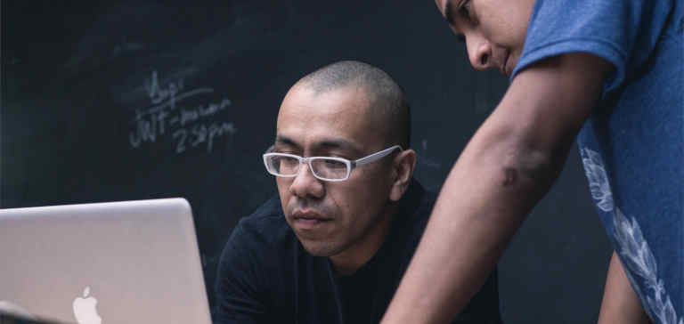 Two men work on a Macbook laptop.