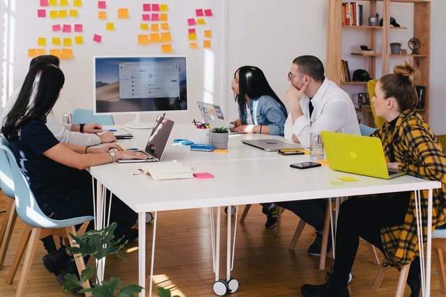 Four people sit around a table with laptops.