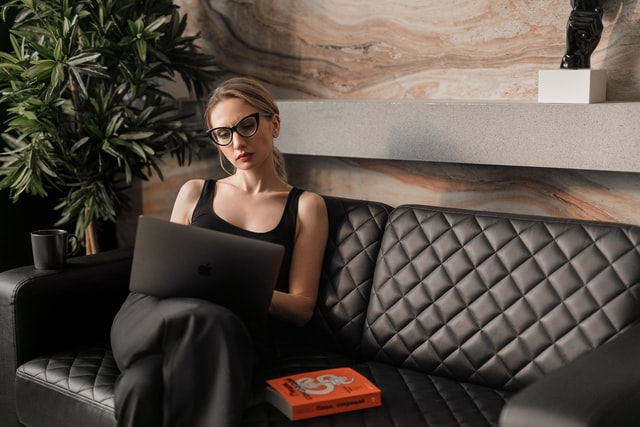 A woman in a black tank top works on a laptop.