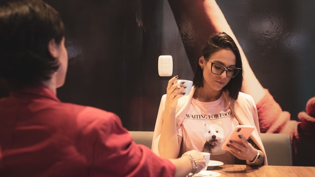 A woman with a pink coat looks at a white smartphone.