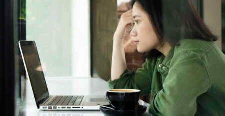 A woman wearing a green jacket looks at a laptop in a cafe.