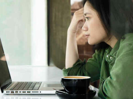 A woman wearing a green jacket looks at a laptop in a cafe.