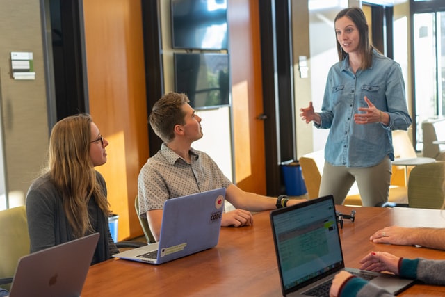 A woman speaks to people gathered around a conference table.