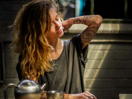 A stressed woman in a gray shirt drinks tea.