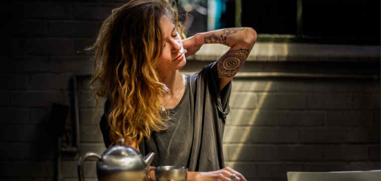 A stressed woman in a gray shirt drinks tea.