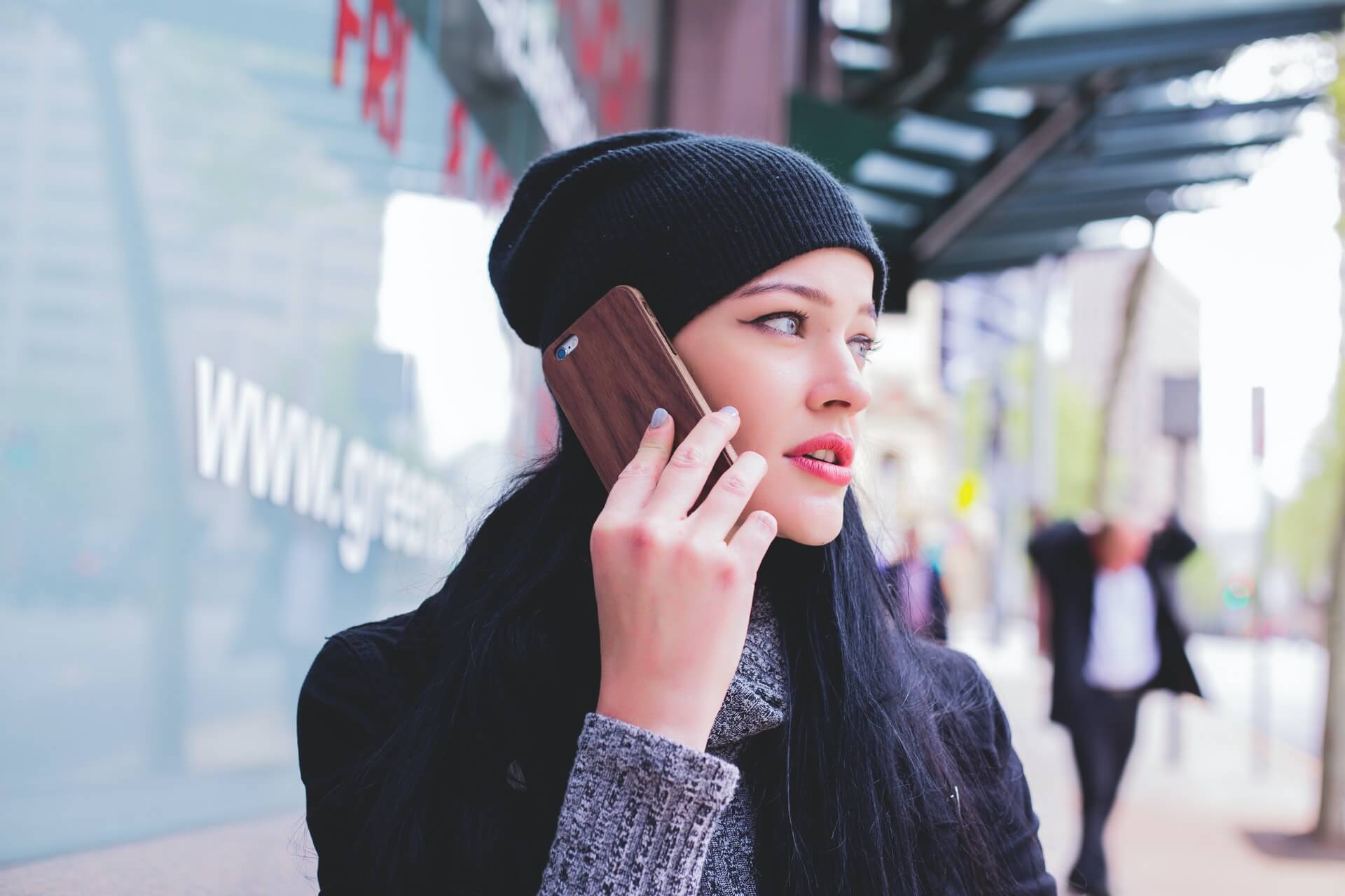 A woman wearing a beanie talks into a smartphone. 