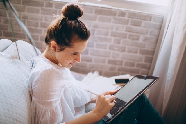 A woman wearing a white shirt works on a tablet.