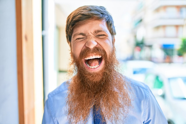 A man in a blue shirt and tie yells at the camera.