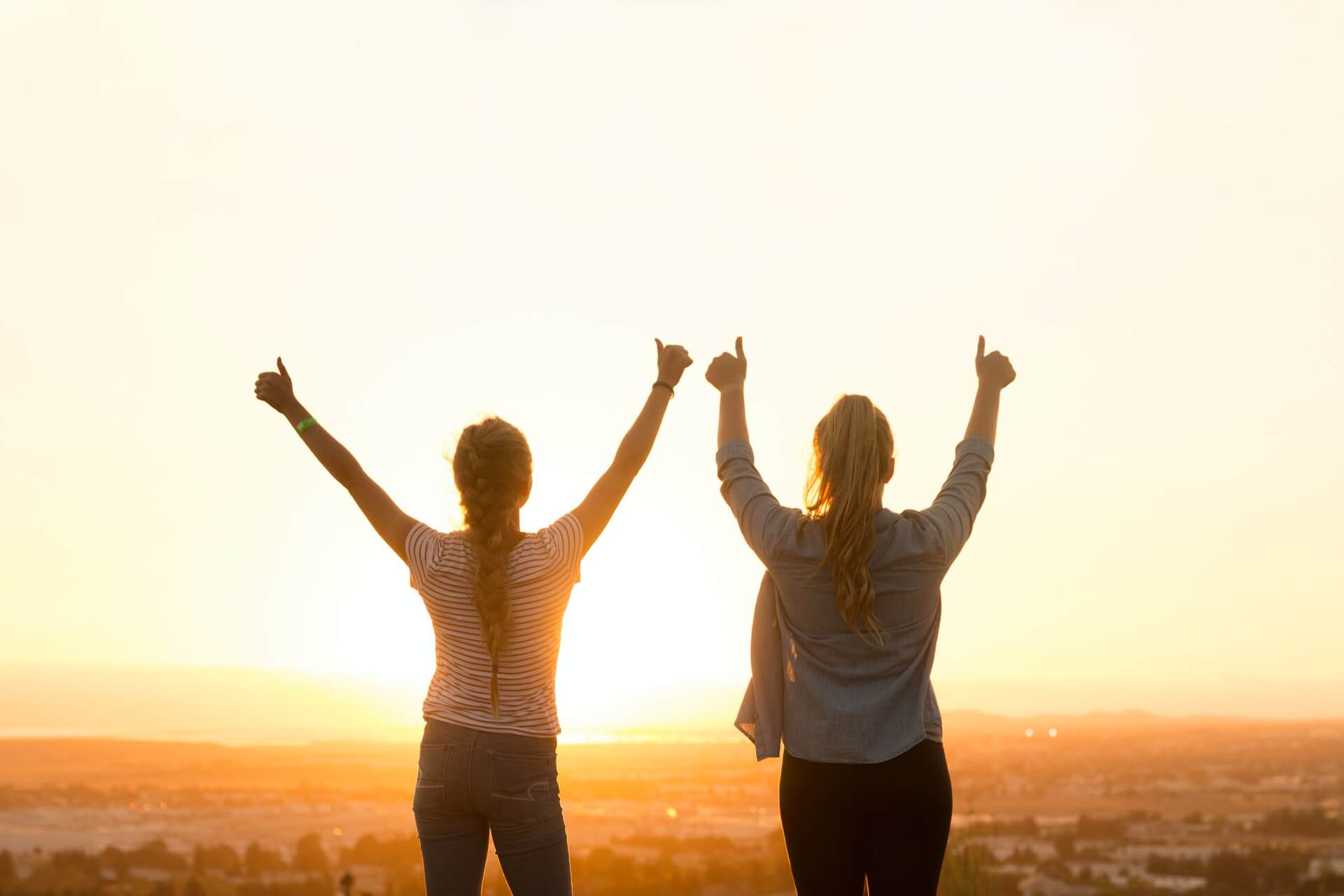 Two women hold their hands up in front of a sunset.