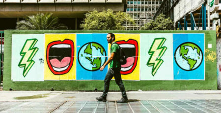 A man wearing a green shirt walks in front of a mural.