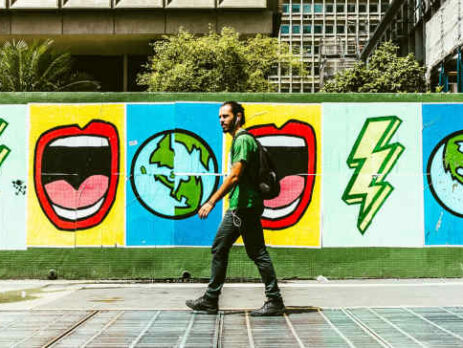 A man wearing a green shirt walks in front of a mural.