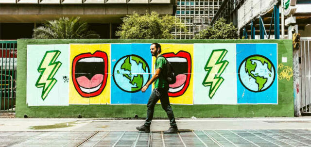 A man wearing a green shirt walks in front of a mural.
