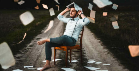 A man wearing suspenders sits in a chair holding a book.