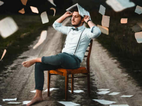 A man wearing suspenders sits in a chair holding a book.