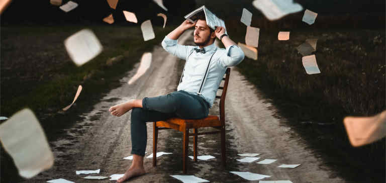 A man wearing suspenders sits in a chair holding a book.