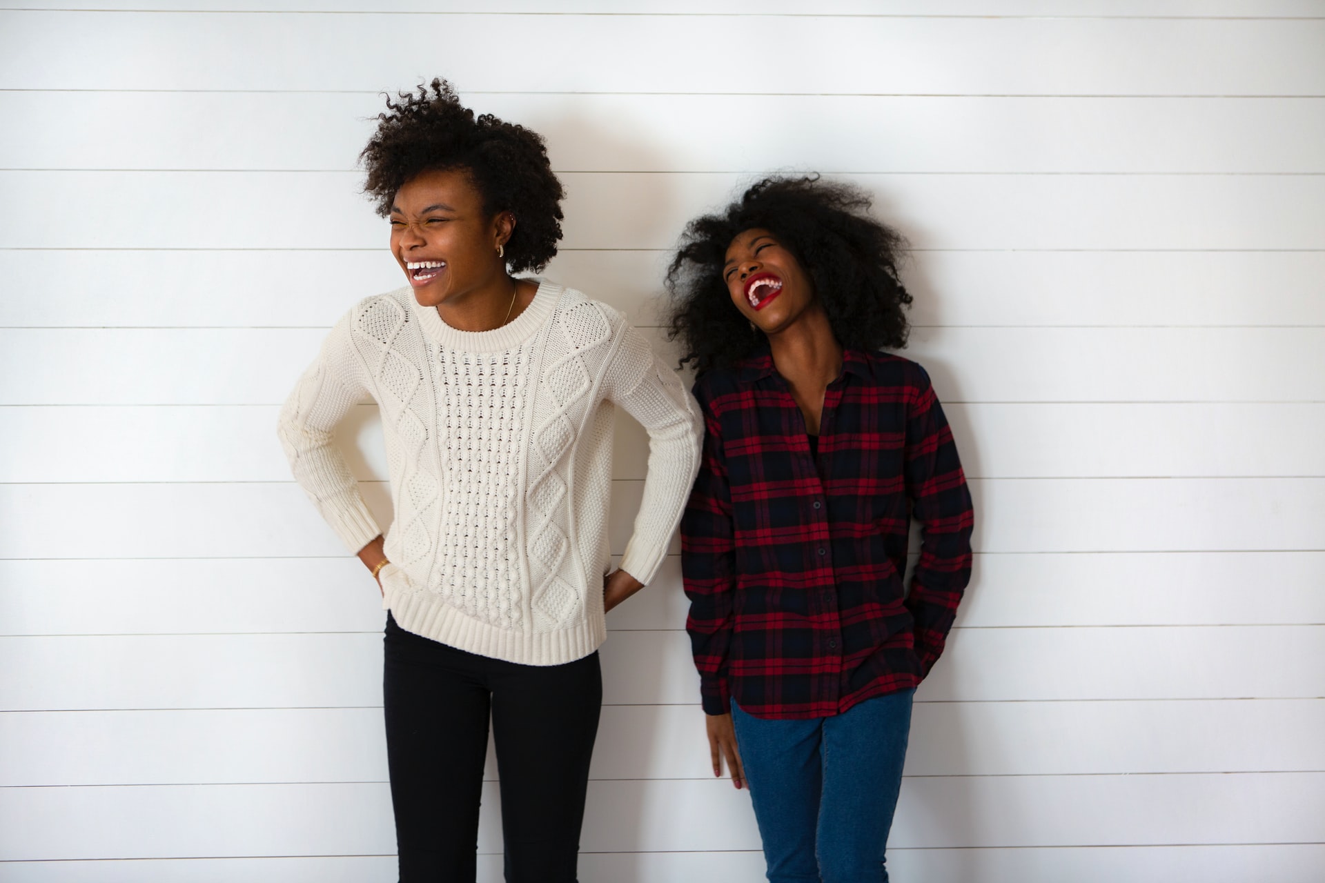 Two women stand against a wall and laugh.