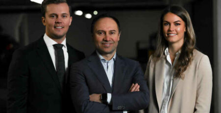 Two men and a woman in business suits stand next to each other.