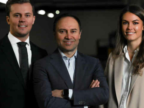 Two men and a woman in business suits stand next to each other.