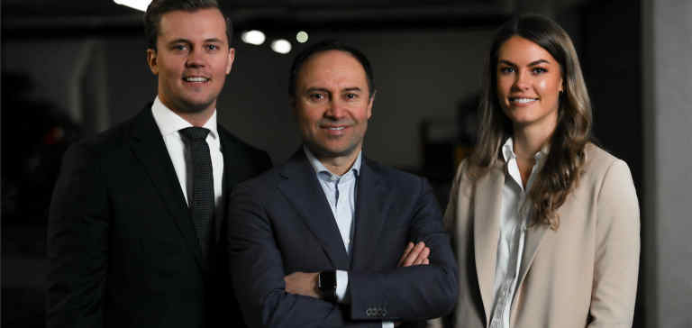 Two men and a woman in business suits stand next to each other.