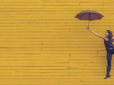 A woman holds a black umbrella near a yellow wall.