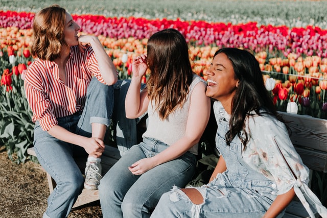 Three women sit outside laughing in the sunshine.