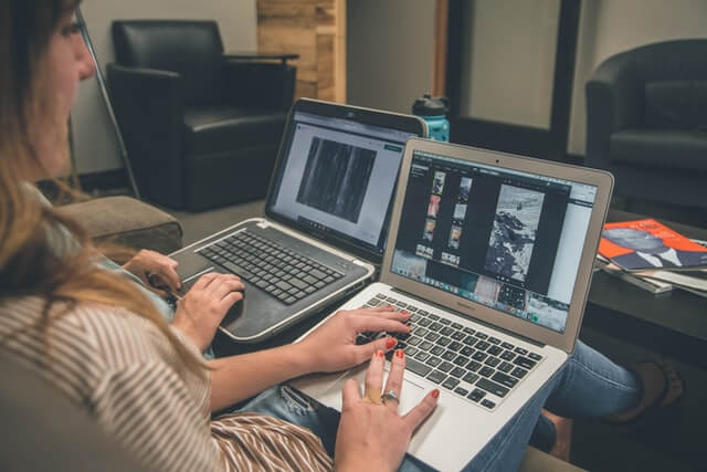 A woman sits near two laptop computers.