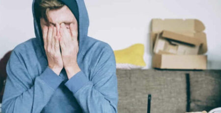 A man in a blue sweater covers his face with his hands.