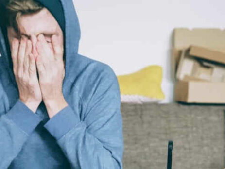 A man in a blue sweater covers his face with his hands.