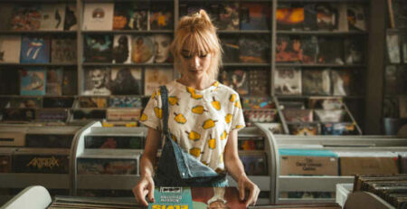 A blonde girl looks at a record in a shop.