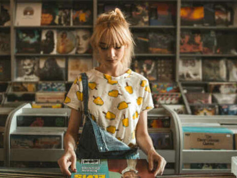 A blonde girl looks at a record in a shop.