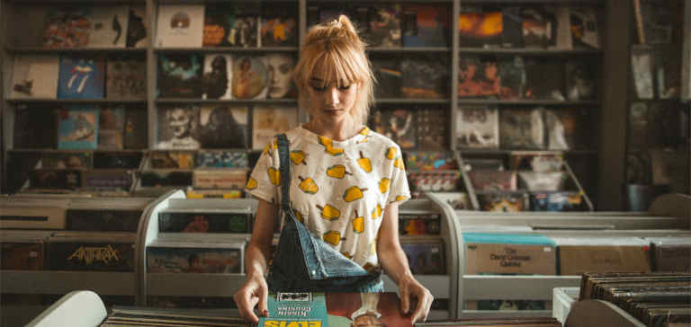 A blonde girl looks at a record in a shop.