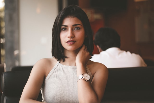 A woman wearing a yellow shirt and wristwatch looks at the camera.