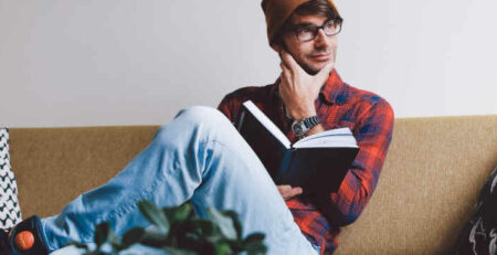 A man in an orange hat sits reading a book.