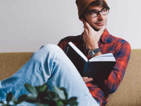 A man in an orange hat sits reading a book.