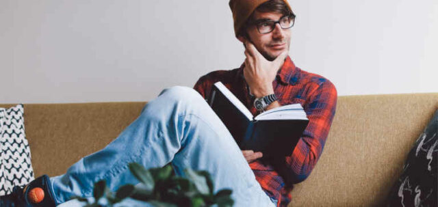 A man in an orange hat sits reading a book.