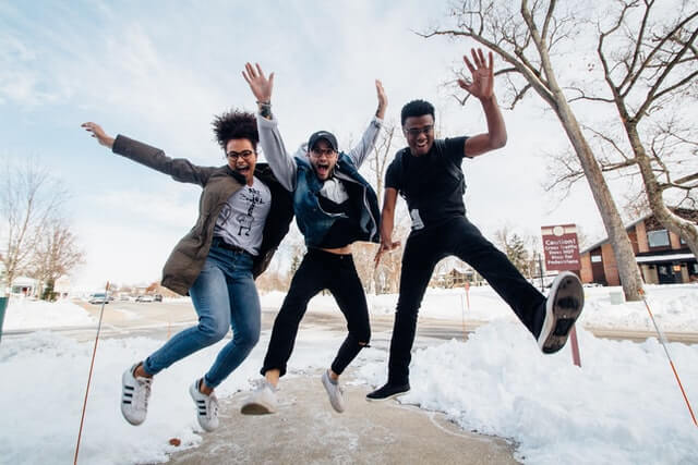 Three people jump in the air in a park full of snow.