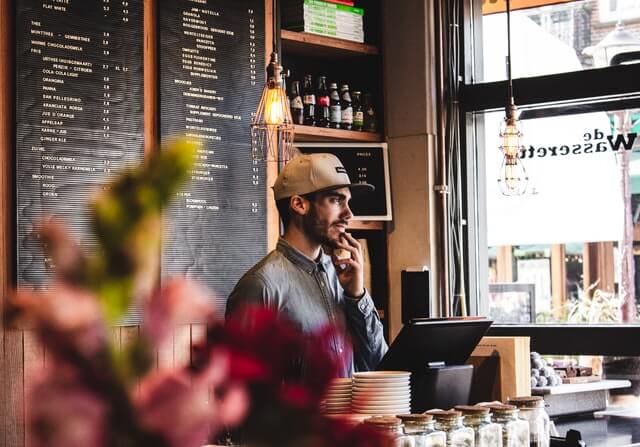 A man wears a hat behind the counter of a small restaurant.