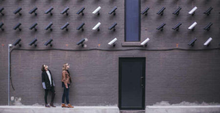 Two women look up at many black and white security cameras.