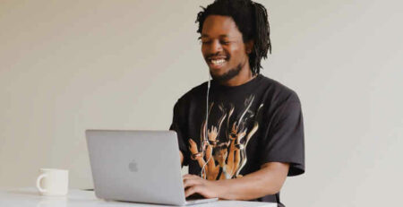 A man in a black t-shirt works on his laptop with a cup of coffee.