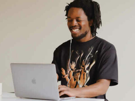 A man in a black t-shirt works on his laptop with a cup of coffee.