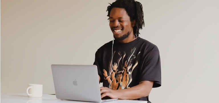 A man in a black t-shirt works on his laptop with a cup of coffee.