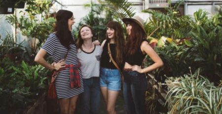 Four women stand talking inside a greenhouse.