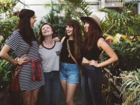 Four women stand talking inside a greenhouse.