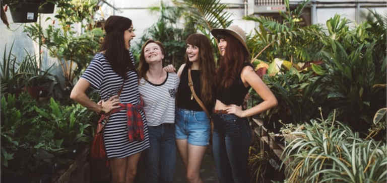 Four women stand talking inside a greenhouse.