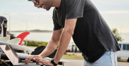 A man in a grey shirt works on a laptop computer outside.