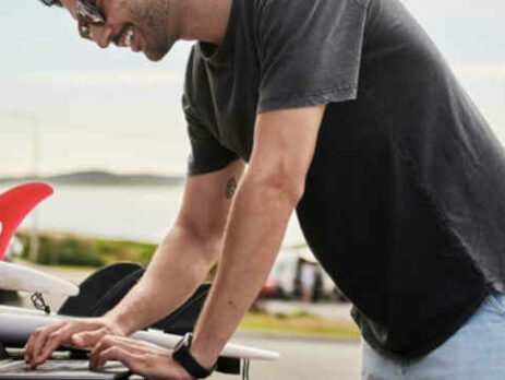A man in a grey shirt works on a laptop computer outside.