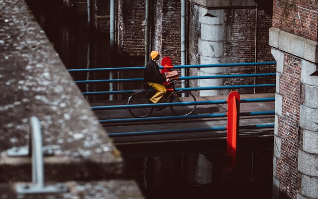 A man in a yellow hat rides a bicycle over a bridge.