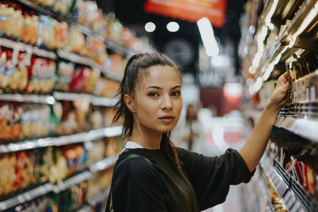 A woman takes something off a shelf at a grocery store.