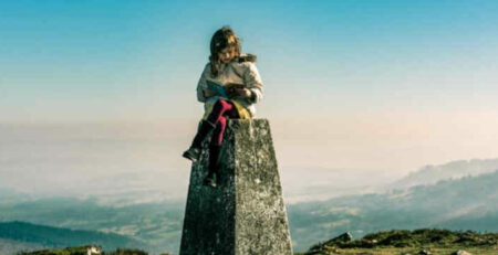 A girl reads a book on top of a pedestal on a mountain.